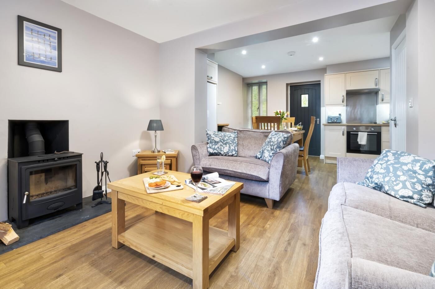 A living room with a fireplace, a sofa, a dining table with food and drink, and a kitchen in the background.
