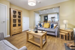 A living room with a sofa, coffee table, and a cabinet. There is a kitchen visible in the background. - 2 Bed in Newby Bridge (oc-b29819) (Newby Bridge)