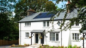 Een wit huis met twee verdiepingen, een zwart dak, zonnepanelen en een klein portaaltje met hangmanden.