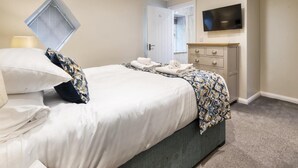 Een hotelkamer met een bed, een aan de muur bevestigde televisie, een dressoir en een raam met jaloezieën.