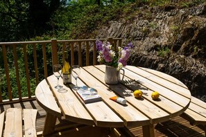 A wooden deck with a round table, a bottle of wine, glasses, a book, a vase with flowers, and lemons. - 2 Bed in Newby Bridge (oc-b29819) (Newby Bridge)