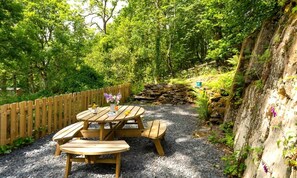 A wooden picnic table with benches, surrounded by a gravel path and a wooden fence. - 2 Bed in Newby Bridge (oc-b29819) (Newby Bridge)