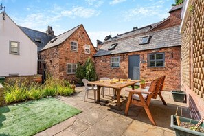 A brick house with a patio, a table with chairs, and a small garden area. - 2 Bed in Whitby (oc-w29863) (Whitby)