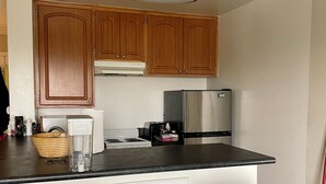 Uma cozinha com armários de madeira, geladeira de aço inoxidável, bancada preta e dois banquetas pretas.