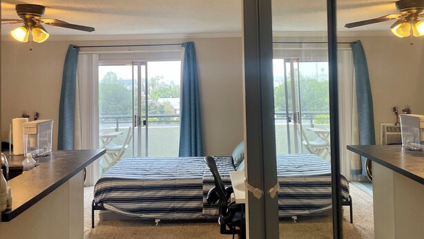 Quarto de hotel com duas camas, uma escrivaninha, uma cadeira, um ventilador de teto e vista para o exterior.