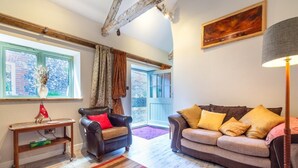 A cozy living room with a leather armchair, a sofa with cushions, a wooden coffee table, and a large window with curtains. - 1 Bed in Trimingham (oc-h29803) (Trimingham)