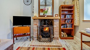 A living room with a fireplace, a television on a wooden stand, a bookshelf, and a window with curtains. - 1 Bed in Trimingham (oc-h29803) (Trimingham)