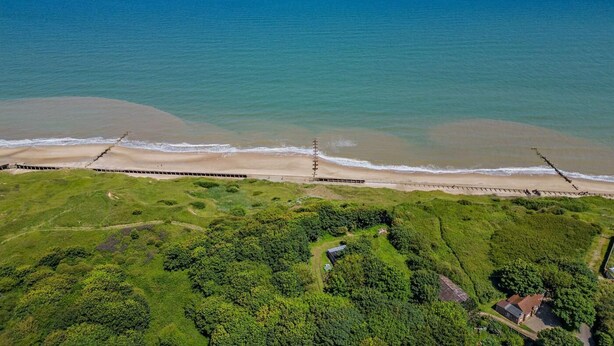 An aerial view of a coastal area with a beach, a wooden walkway, and dense greenery. - 1 Bed in Trimingham (oc-h29803) (Trimingham)