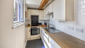 Cozinha compacta com armários brancos, bancada de madeira, forno embutido e janela que proporciona luz natural.
