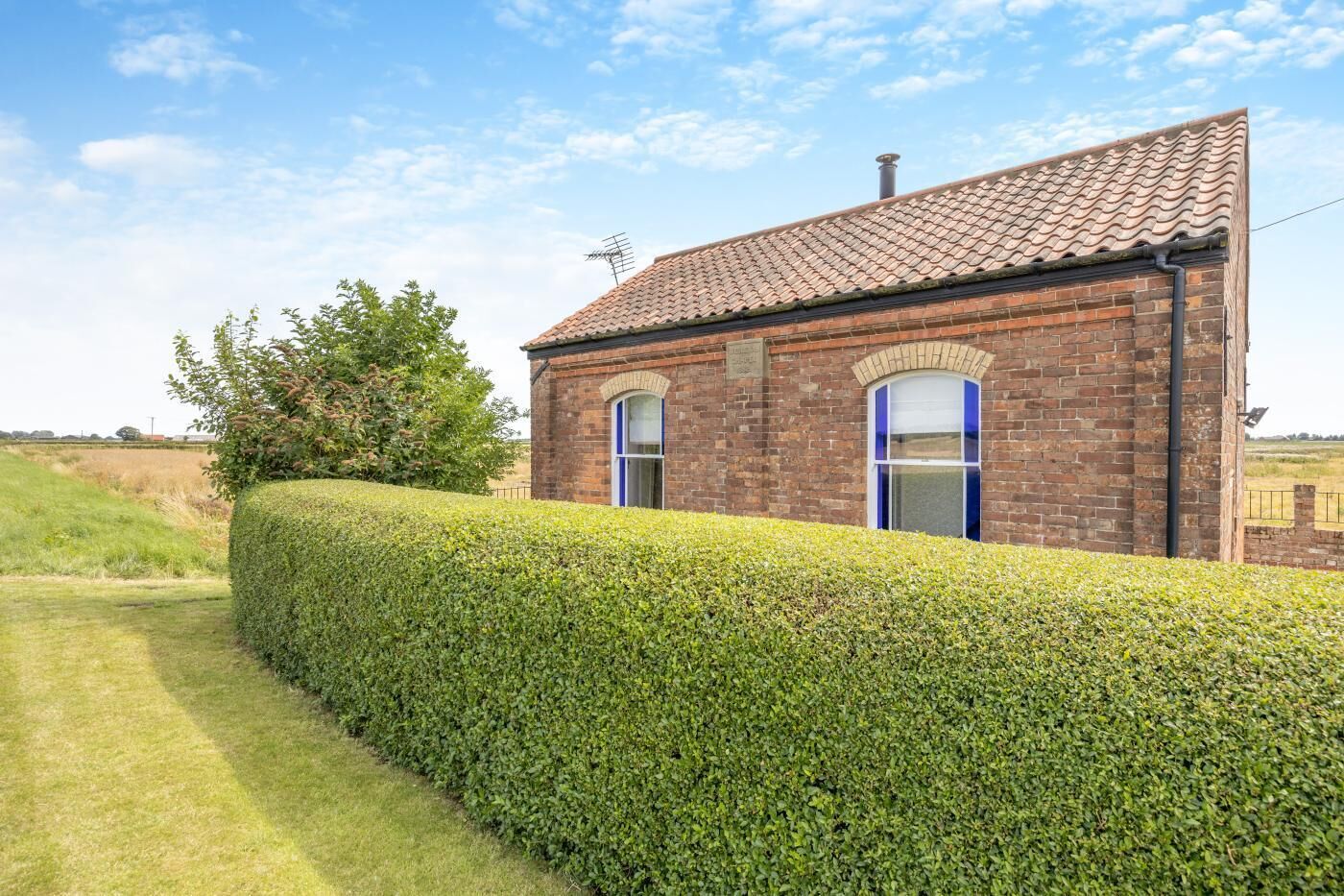 A brick house with a tiled roof, a hedge in front, and a clear sky.
