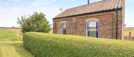 A brick house with a tiled roof, a hedge in front, and a clear sky.