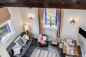 A room with a black leather sofa, a small table with a vase of flowers, and a window with curtains. - 1 Bed in Toynton All Saints (oc-s29840) (Toynton All Saints)