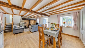 A spacious living area with a stone fireplace, wooden beams, and a dining table set for breakfast. - 3 Bed in Brithdir (oc-b29844) (Brithdir and Llanfachreth)