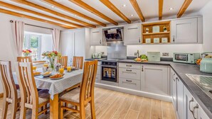 A modern kitchen with wooden beams, a dining area with a table set for breakfast, and a view of the outdoors. - 3 Bed in Brithdir (oc-b29844) (Brithdir and Llanfachreth)