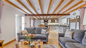 A modern living room with grey sofas, a wooden coffee table with tea set, and a kitchen in the background. - 3 Bed in Brithdir (oc-b29844) (Brithdir and Llanfachreth)