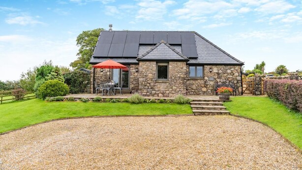 A stone house with a gravel driveway, a patio with outdoor furniture, and a red umbrella. - 2 Bed in Reynoldston (oc-l29892) (Reynoldston)