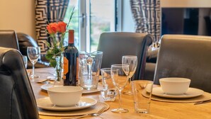 A dining table set with plates, bowls, glasses, and a bottle of wine, with a vase of flowers and a window in the background. - 2 Bed in Reynoldston (oc-l29892) (Reynoldston)