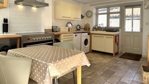 Een praktische keuken met een kookplaat, oven, wasmachine en een eethoek met een tafel.