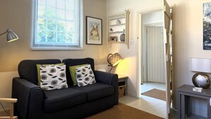 Een moderne woonkamer met een zwarte bank, een bijzettafeltje, een lamp en een deur naar een andere kamer.