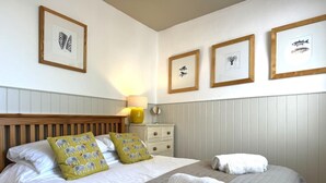Een keurig opgemaakt bed met kussens, een bedlampje en ingelijste foto’s aan de muur.
