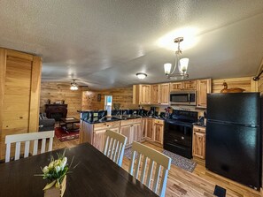 Una cocina compacta con armarios de madera, un refrigerador negro, un microondas y una estufa. Hay un comedor con una mesa y sillas.