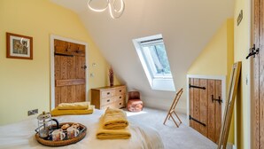 Ein gemütliches Schlafzimmer mit schrägen Wänden, Holzschränken, einem Bett mit einer Handtuchkorb und einem Oberlicht.