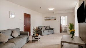 Ein Wohnzimmer mit einem grauen Sofa, einem kleineren grauen Sofa, einem Couchtisch und einem an der Wand montierten Fernseher.