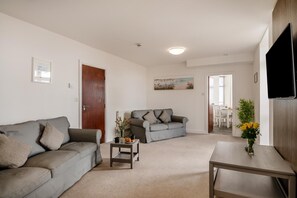 Ein Wohnzimmer mit einem grauen Sofa, einem kleineren grauen Sofa, einem Couchtisch und einem an der Wand montierten Fernseher.