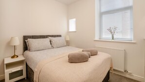 Ein Schlafzimmer mit einem Bett, Nachttischen, einem Fenster mit Jalousien und einer Heizung.