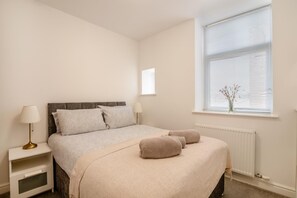 Ein Schlafzimmer mit einem Bett, Nachttischen, einem Fenster mit Jalousien und einer Heizung.