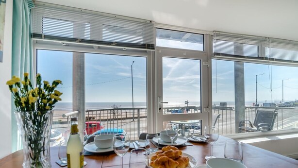 A dining table with plates, glasses, and a vase of flowers, overlooking a beach and airport. - 2 Bed in Bridlington (oc-o29896) (Bridlington)