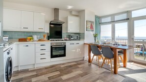 A modern kitchen with white cabinets, a gas stove, an oven, and a dining area with a table and chairs. - 2 Bed in Bridlington (oc-o29896) (Bridlington)