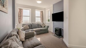 A living room with a grey sofa, a flat-screen TV mounted on the wall, and a fireplace. - 2 Bed in Bridlington (oc-o29897) (Bridlington)