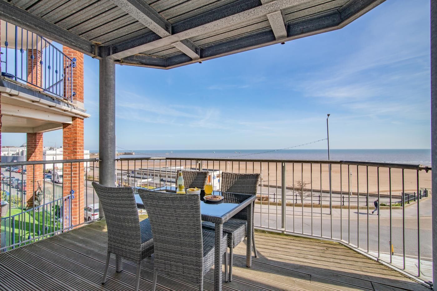 Un balcón con muebles de mimbre, una mesa con bebidas y vista a la playa y al océano.