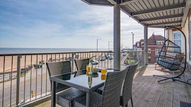 Een balkon met rieten meubels, een hangstoel en een tafel met drankjes.
