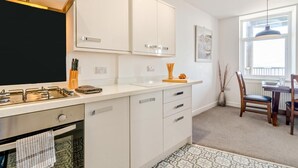 Een moderne keuken met witte kastjes, een gasfornuis en een eethoek met een tafel en stoelen.