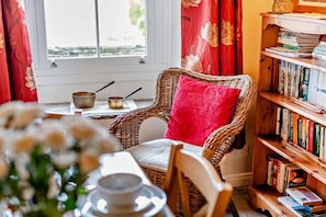 A wicker chair with a red pillow, a bookshelf with books, and a window with curtains. - 3 Bed in Gunnerside (oc-e26693) (Ivelet)