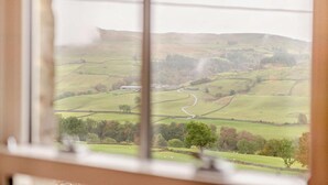 A view of rolling hills and a winding road from a window with blinds. - 3 Bed in Gunnerside (oc-e26693) (Ivelet)