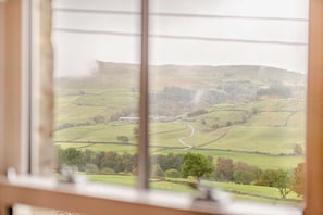 A view of rolling hills and a winding road from a window with blinds. - 3 Bed in Gunnerside (oc-e26693) (Ivelet)