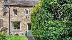 Una casa di pietra con un piccolo giardino, un’antenna parabolica e un siepe.