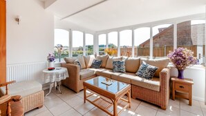 A sunlit living room with a sofa, coffee table, and wicker furniture. - 4 Bed in Woolage Green (oc-f29907) (Woolage Green)