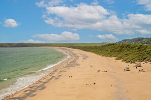 Ein weiter Sandstrand mit klarem, blauem Wasser, einige Spaziergänger und ein Rettungsturm in der Ferne.