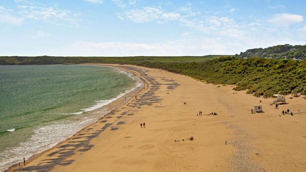 Une vaste plage de sable fin, offrant une vue dégagée sur l’océan et un paysage vallonn é en arrière-plan.