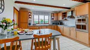 Une cuisine avec des meubles en bois, une table à manger avec des chaises, une grande fenêtre et un four encastré.