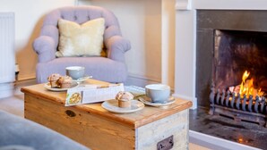 Una sala de estar acogedora con chimenea, una mesa de centro de madera con pasteles y un menú, y un sillón cómodo.