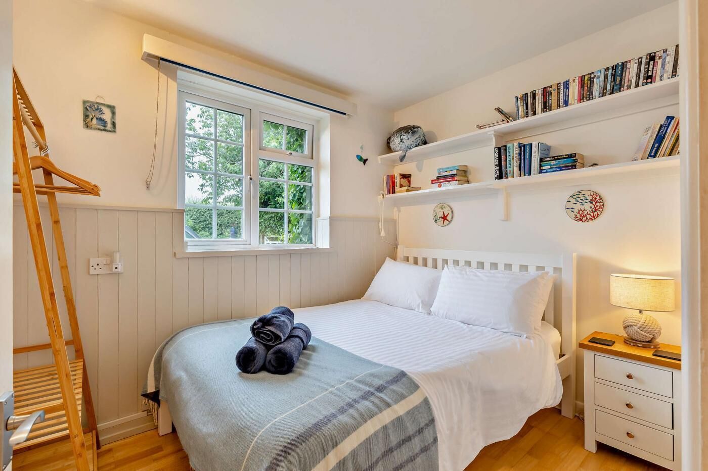 Un dormitorio ordenado con una cama, una mesita de noche, una estantería y una ventana.