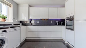 Una cocina moderna con armarios blancos, lavavajillas, lavadora, horno empotrado y una ventana con una planta.