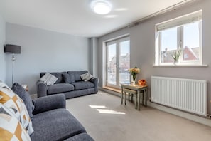 Un salon moderne avec des canapés gris, une petite table sur laquelle on a posé des fruits et un radiateur.