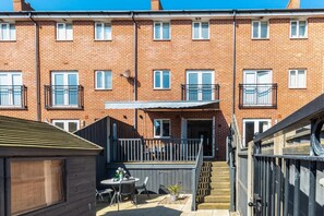 Un immeuble d’appartements en briques avec un petit patio, une table et des chaises, et un pot de fleurs.
