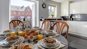 Una cocina moderna con armarios blancos, una mesa de comedor lista para el desayuno y vistas a un edificio de ladrillo rojo.